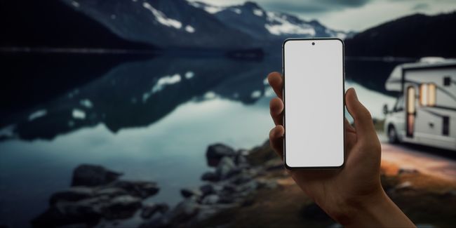 Hand holding a cell phone in front of an RV and mountain scene