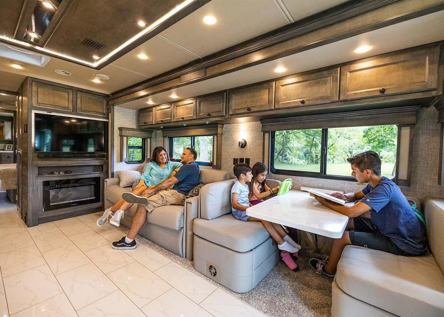 Inside a Tiffin RV, with two parents sitting on a couch by the fireplace and three children sitting at the dinette