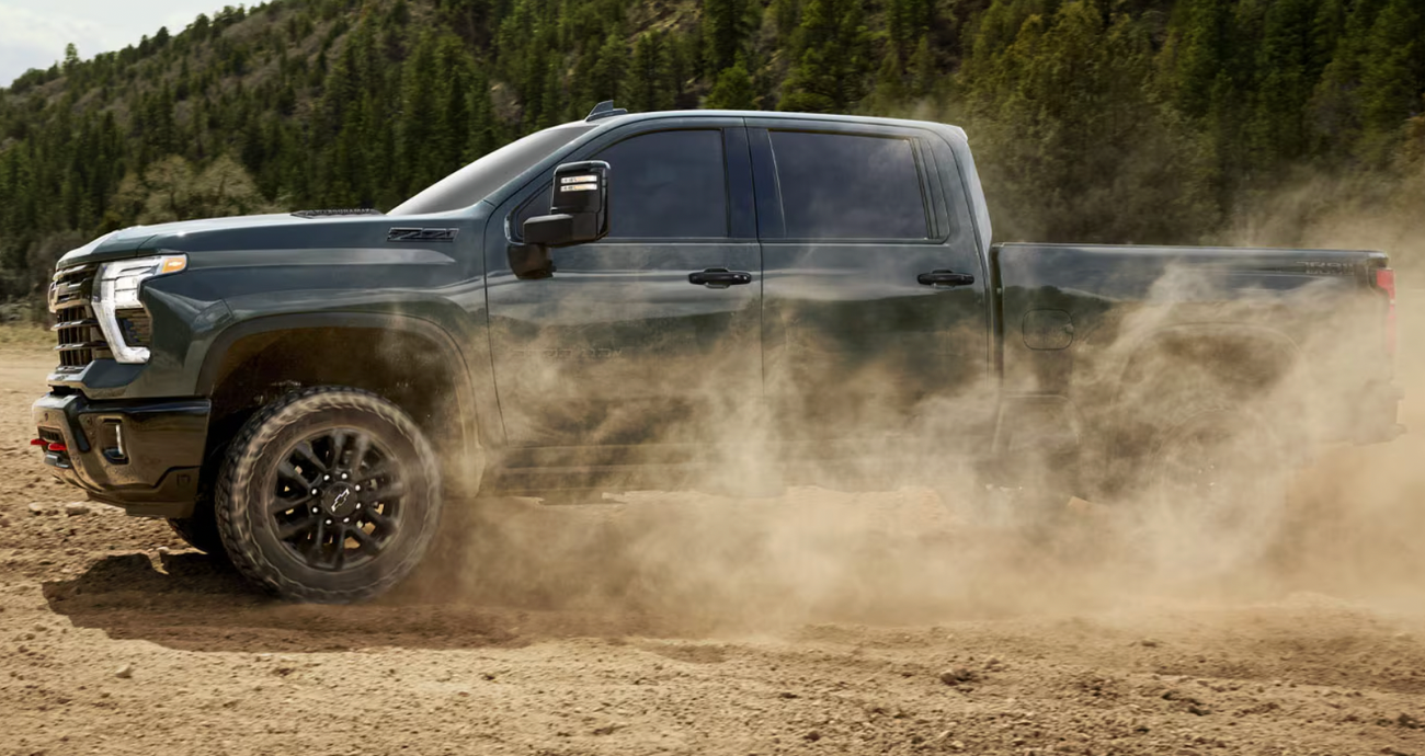 A dark green Chevy Silverado truck surrounded by dust