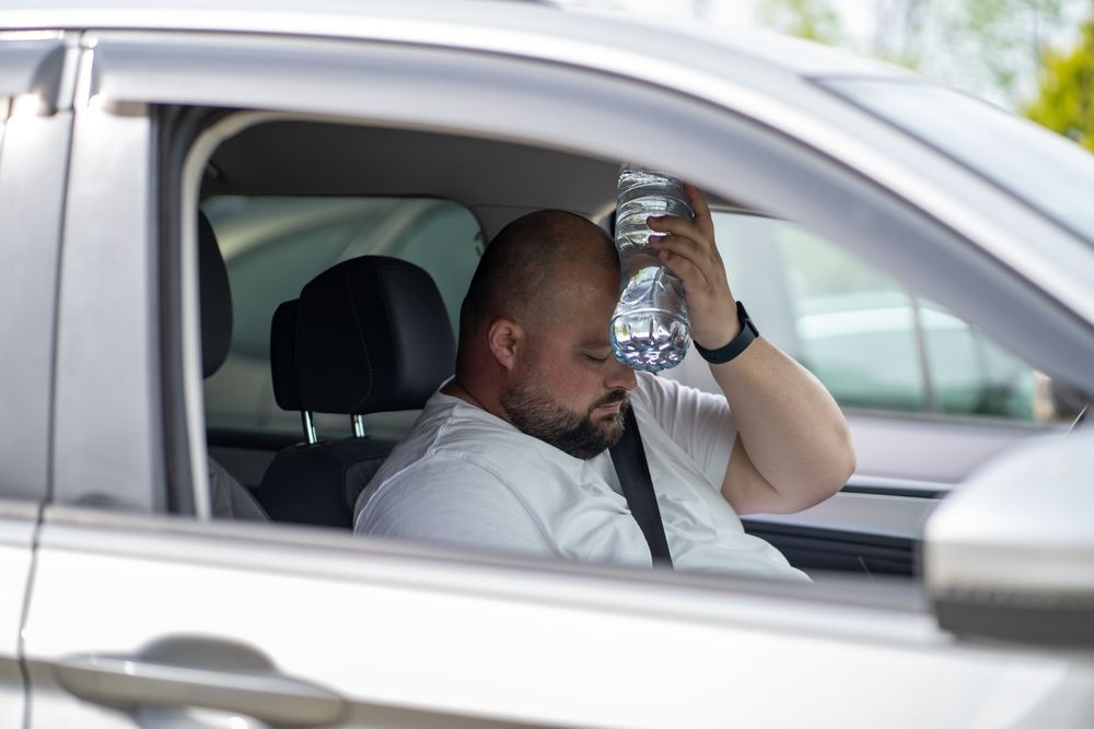 Man uses a cool water bottle to cool off in a car