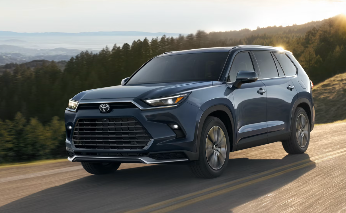 A Toyota Grand Highlander drives past trees and mountains