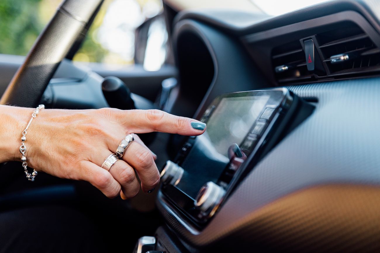 A hand with dark nail polish and rings reaches for a car radio