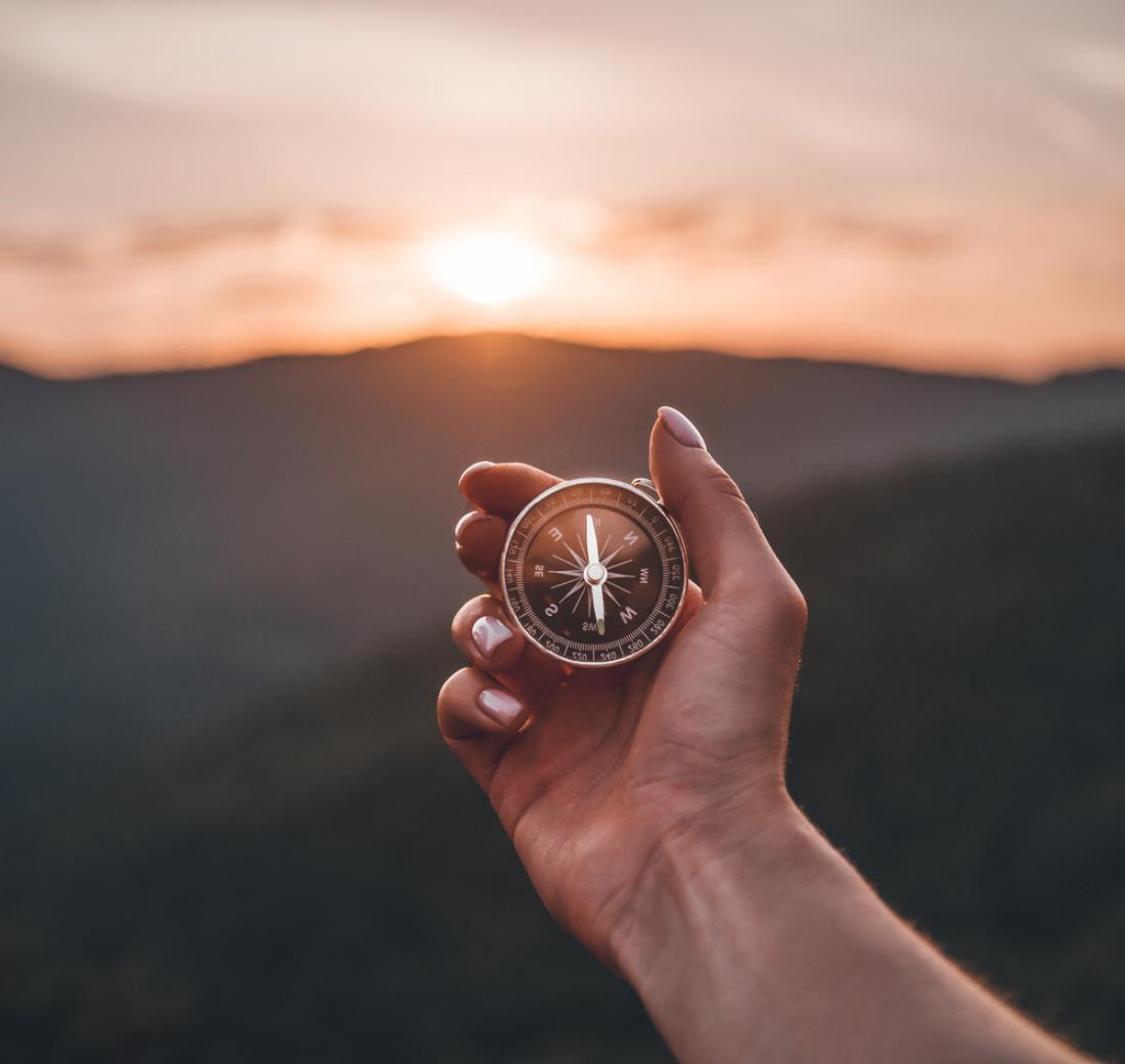 Hand holding a compass in front of a mountain scene