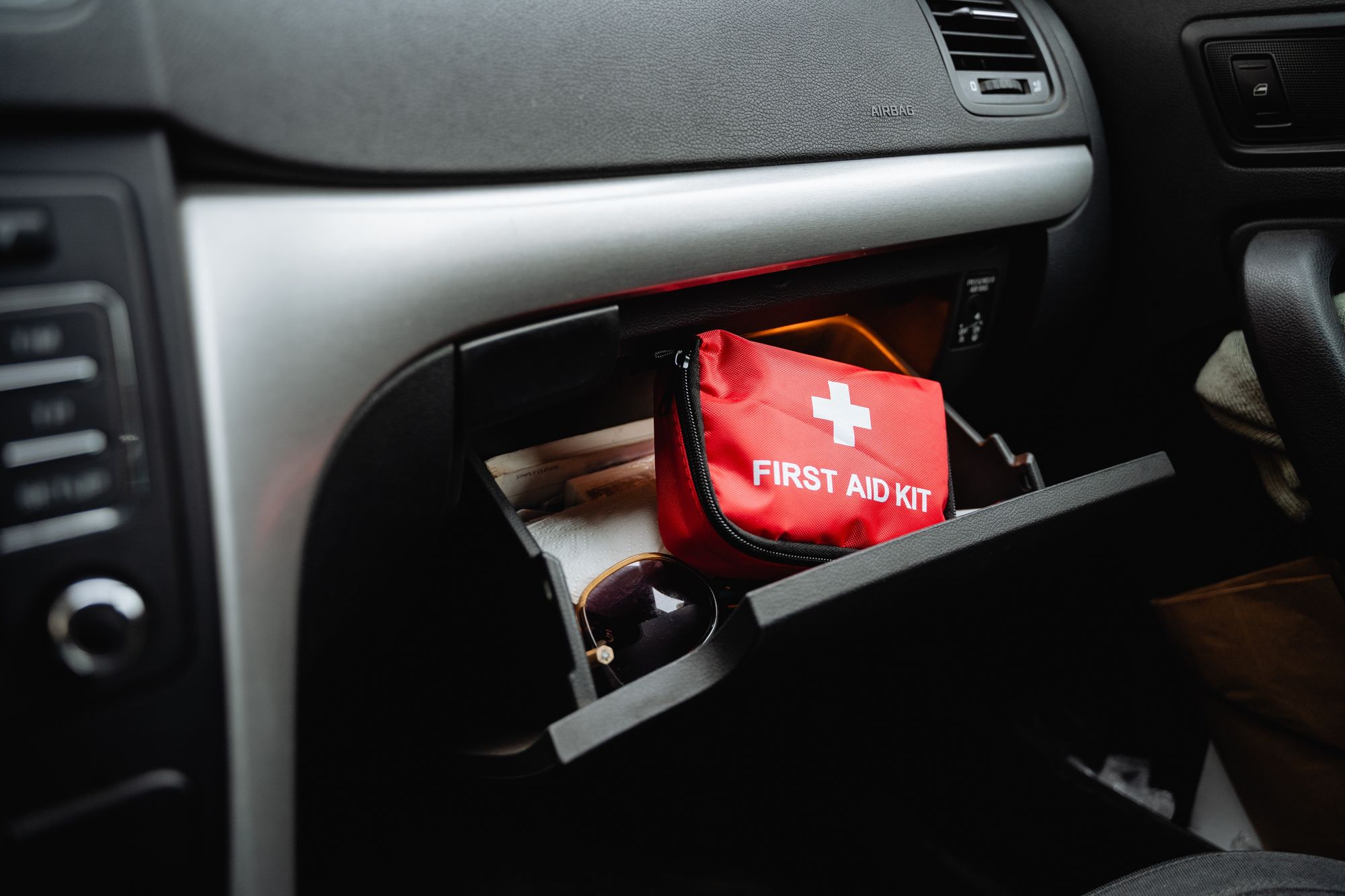 A red first aid kit bag in the glove compartment of a car