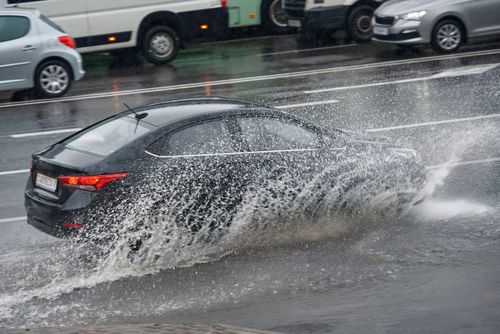 A black sedan drives through a puddle