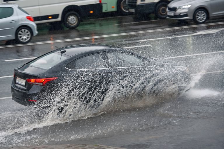 A black sedan drives through a puddle