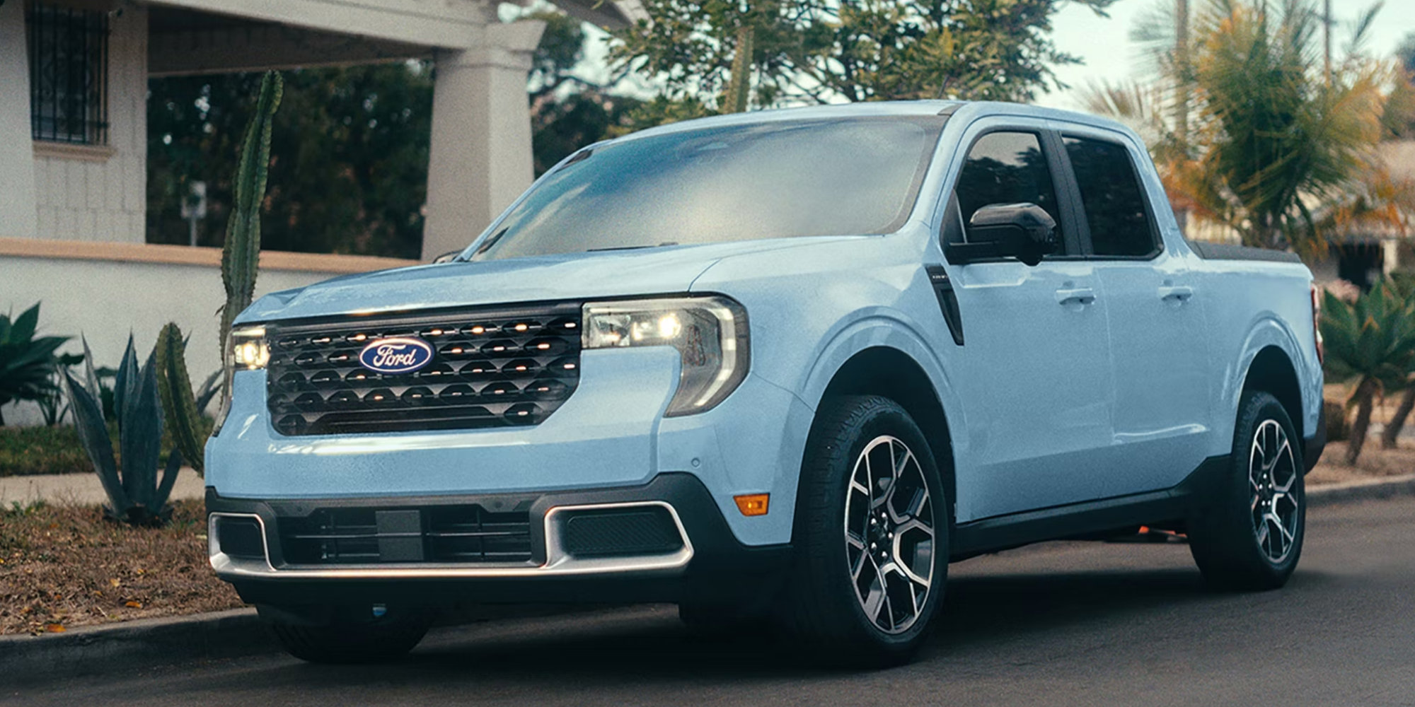 A light blue Ford Maverick parked near cacti and palm trees