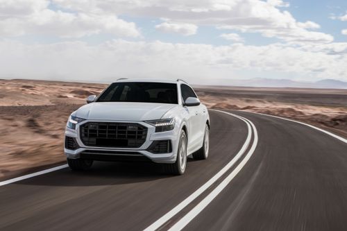 A white SUV drives on a road past a sandy area