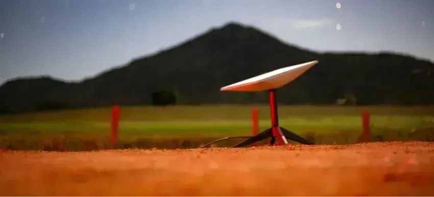 Portable Starlink satellite dish on a tripod in a desert landscape under a star-filled night sky with mountains behind it