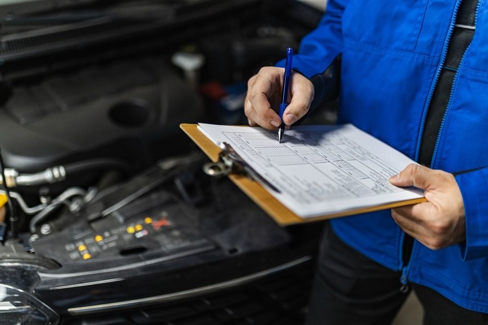 Mechanic writing on a clipboard in front of a car with open hood