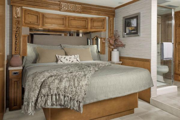 King size bed with neutral decor and a fish-patterned pillow inside a Class A Luxury RV