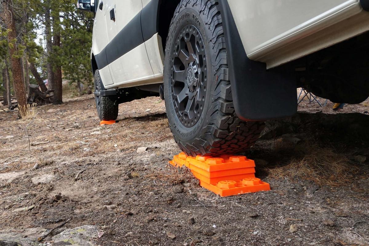 Close up view of a campervan tire parked on top of an orange leveler in the dirt