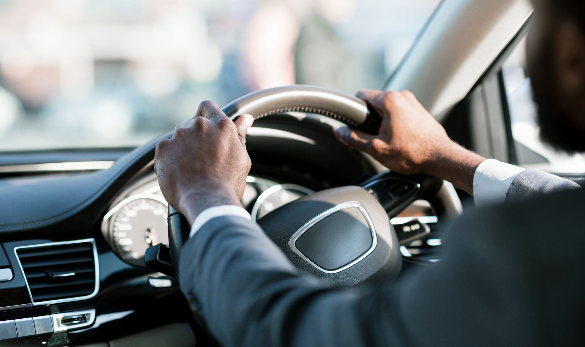 Someone wearing a suit grips a steering wheel