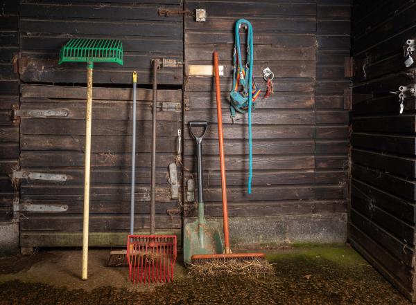 Rake, hose, and various other barn tools leaning against a wooden barn wall