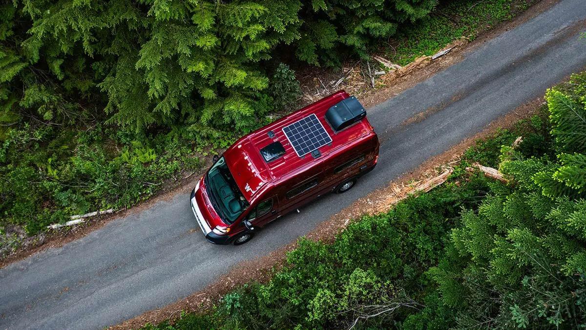 Overview of a red Winnebago Solis driving on a forested road