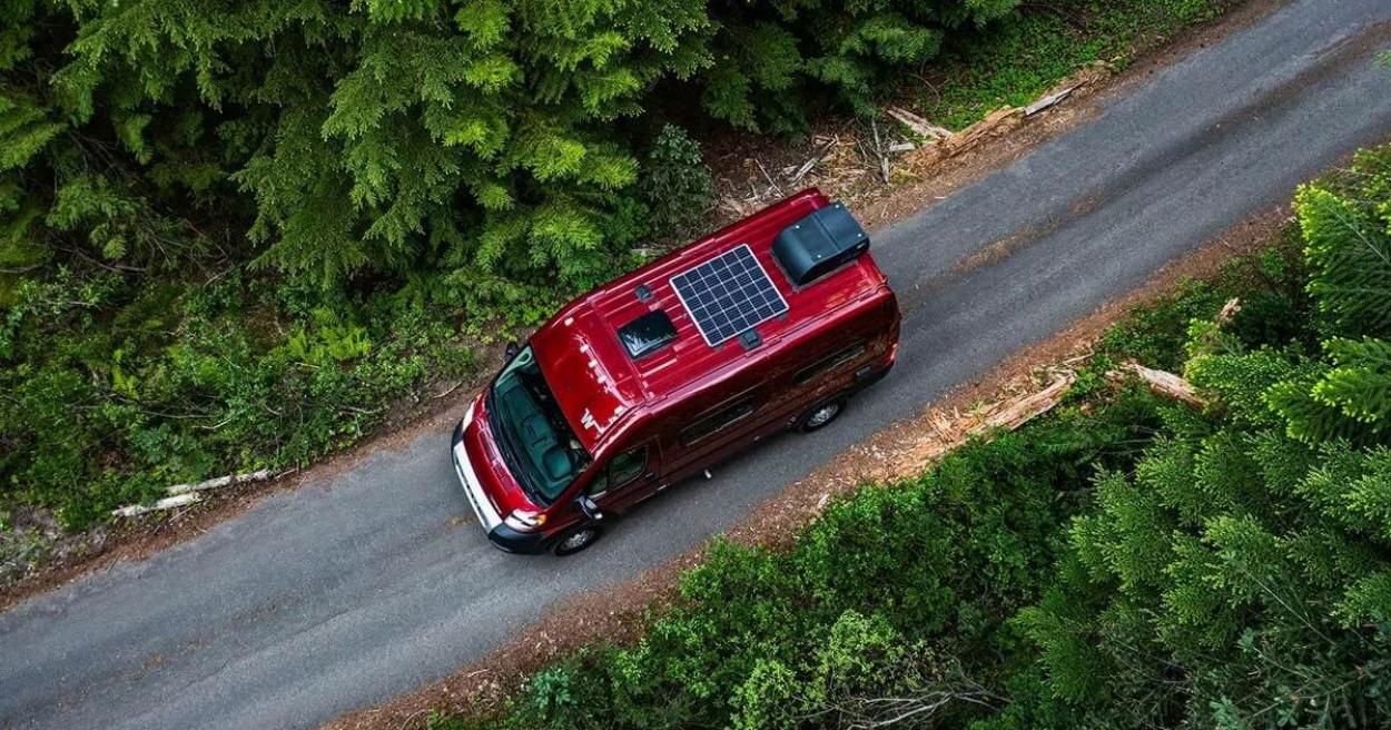 Overview of a red Winnebago Solis driving on a forested road