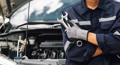 A mechanic holds two wrenches in front of a car