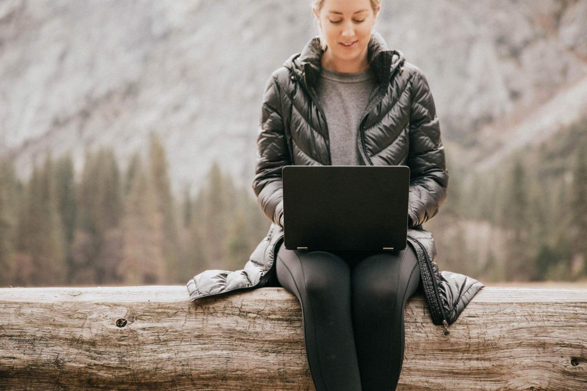Woman sitting on a log working on a black laptop