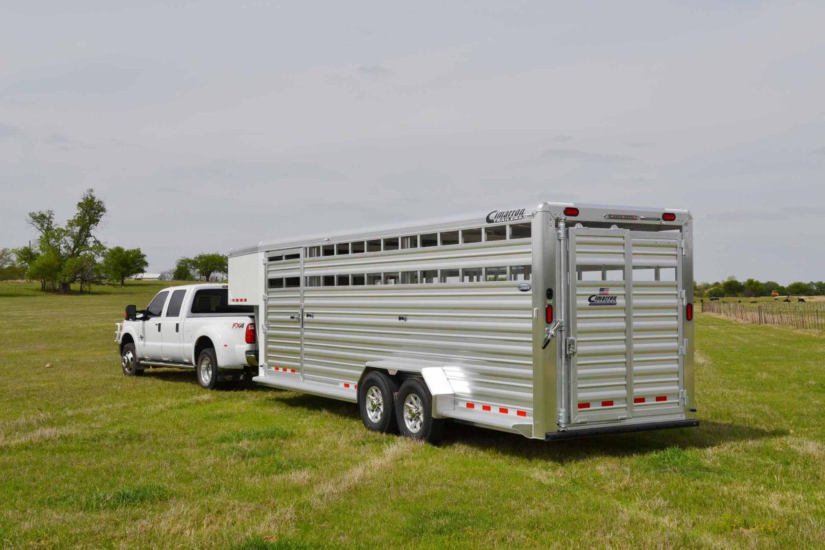 Livestock trailer towed by a white pickup truck parked on a grassy field