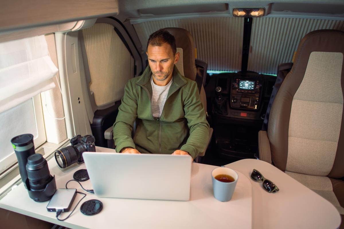 Man working on a laptop with camera equipment beside him in an RV