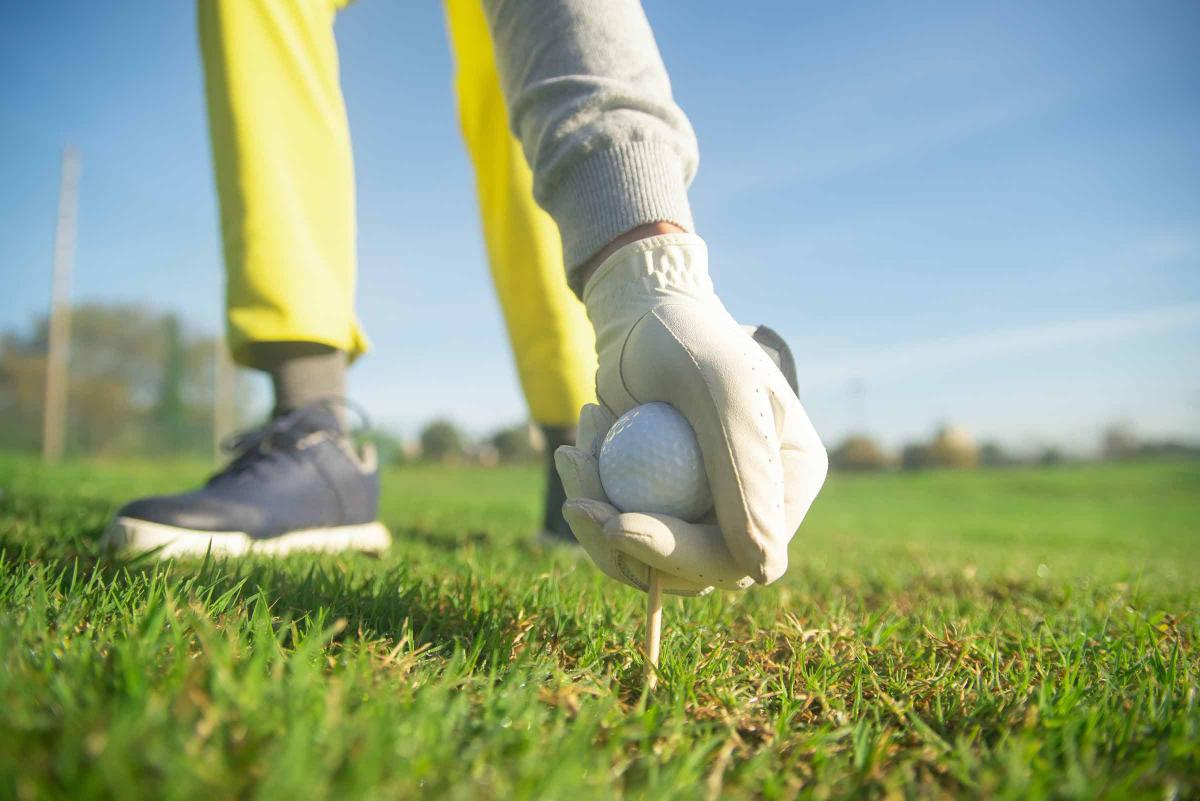Gloved hand places a golf ball and tee in the ground
