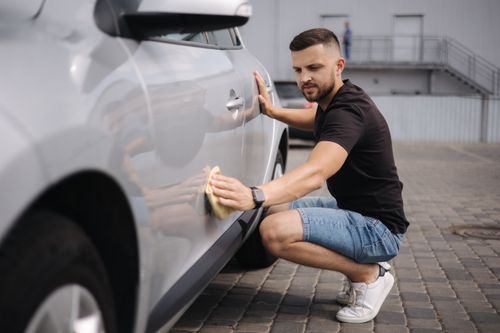 A man crouches on the ground scrubbing a gray vehicle