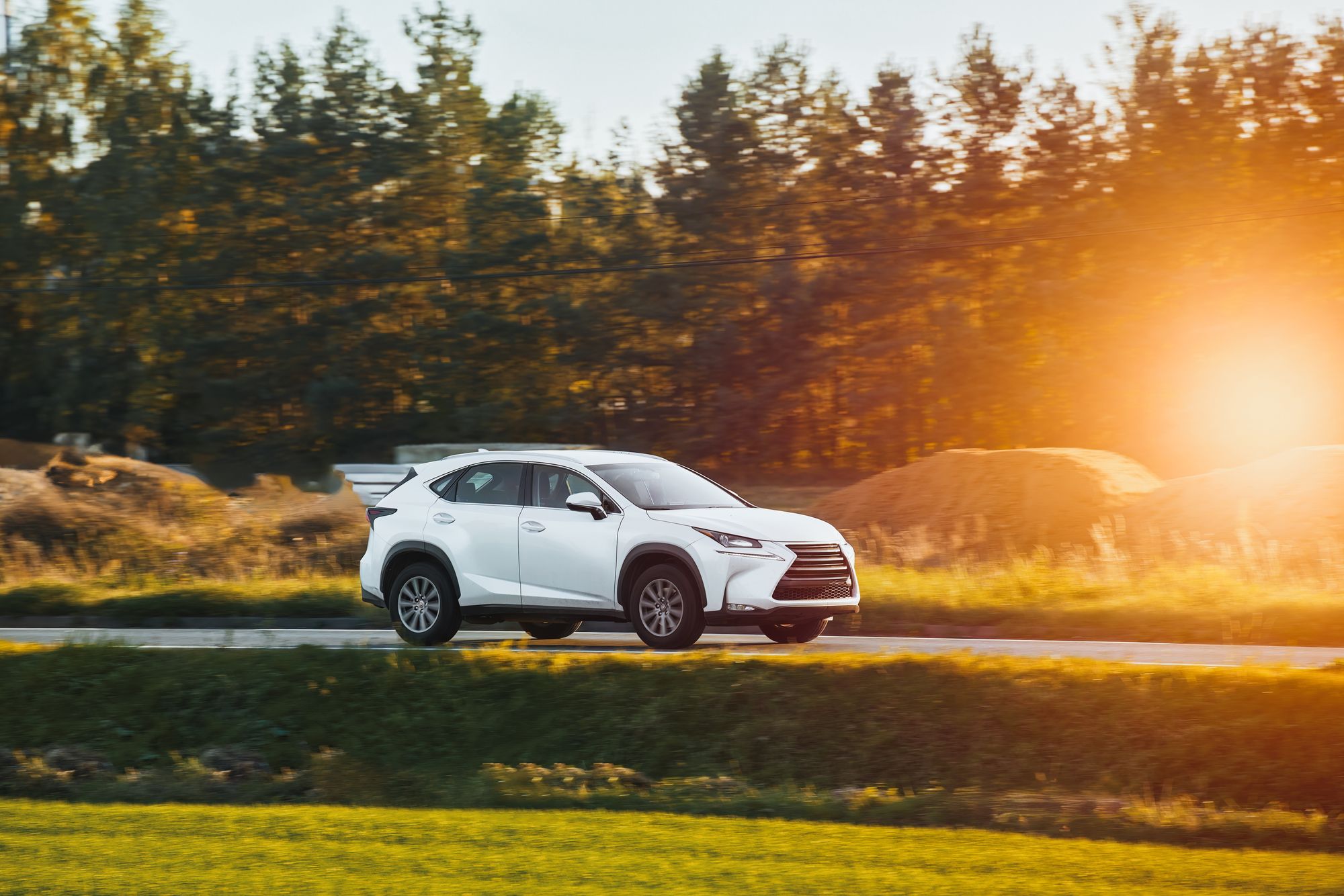 A white SUV drives in front of trees