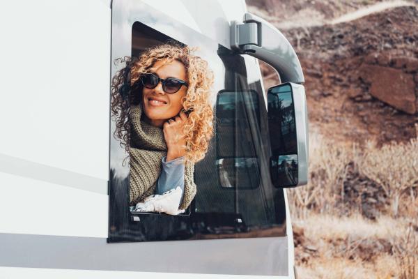 Woman leaning out of the front side window of a Class A RV, smiling and holding her hair back