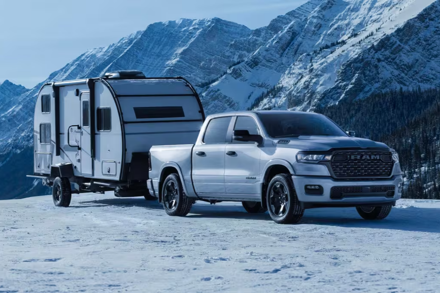 The 2026 Ram 1500 pickup with a trailer attached, parked in the mountains, showcasing its strong towing capacity.
