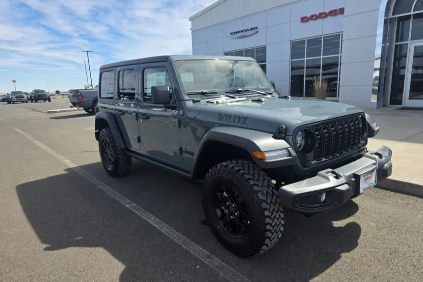 2026 Jeep Wrangler 4-Door Willys in Anvil Clear-Coat showing off its gloss black grille rings, high-clearance Rubicon flares, and aggressive mud-terrain tires.