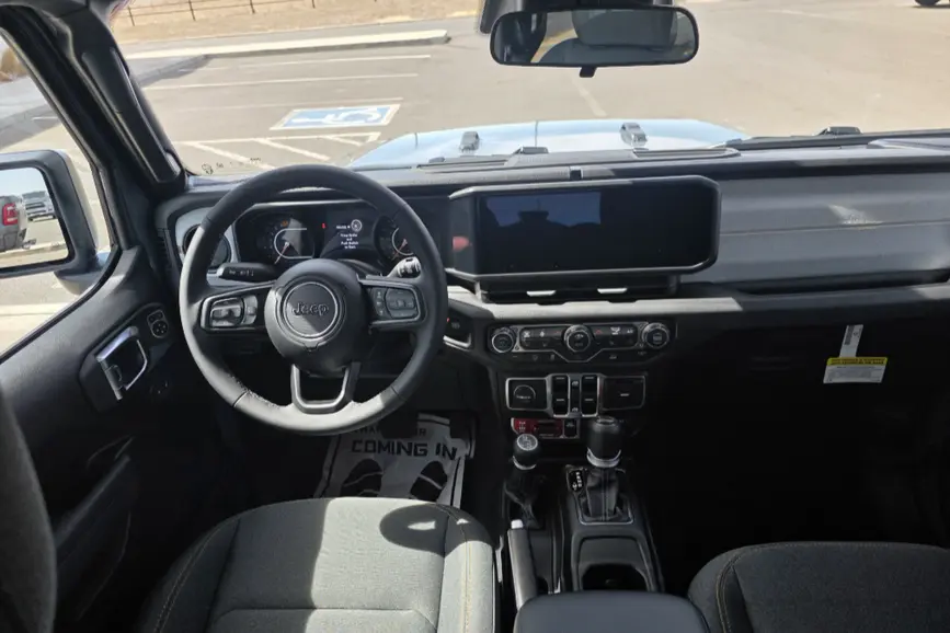 Interior view of the 2026 Jeep Wrangler dashboard highlighting the massive 12.3-inch primary display screen and rugged center console switch controls.