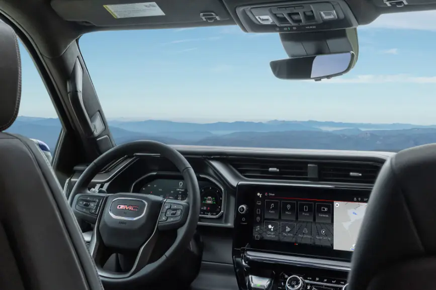 Interior view of the 2026 GMC Sierra digital cockpit displaying a large infotainment touchscreen with Google built-in navigation and a view of mountains through the front windshield.