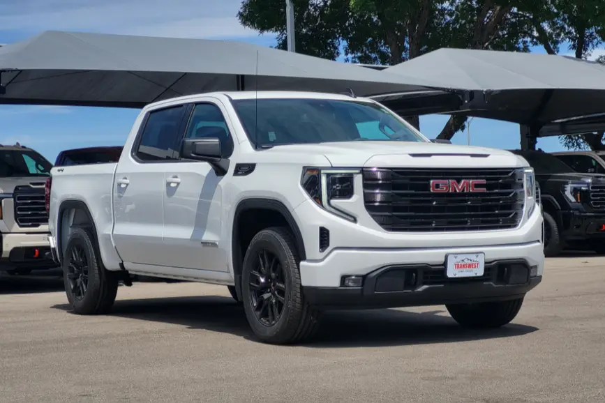 A new white 2026 GMC Sierra 1500 Elevation crew cab truck with black wheels parked on a dealership lot under a sunshade awning.