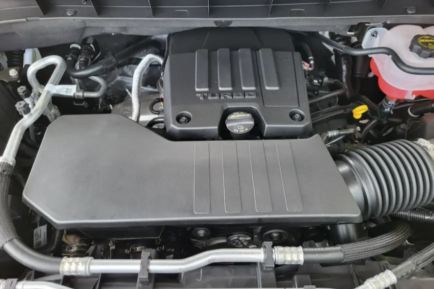 Top-down view of a 2026 GMC Sierra 1500 TurboMax engine bay highlighting the black plastic protective engine cover with stamped "TURBO" lettering.