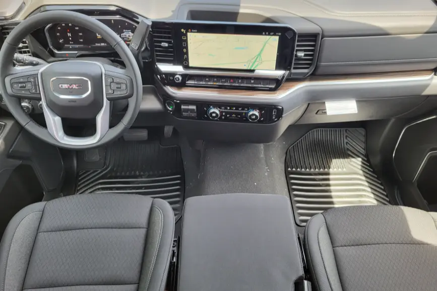 Interior view of a 2026 GMC Sierra 1500 Elevation cabin featuring black cloth seats, a digital instrument cluster, and a wide infotainment touchscreen displaying a navigation map.