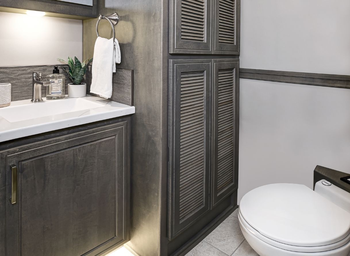 Bathroom of the 2026 Renegade Explorer with a vanity sink, storage cabinets, and a modern toilet. Neutral tones and built-in shelving add style and function.