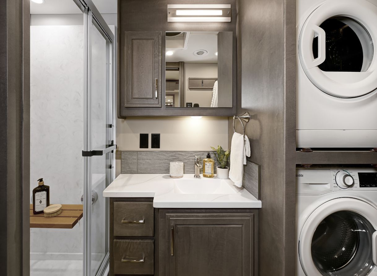 Bathroom of the 2026 Renegade Explorer with vanity, storage, and glass-door shower. A stacked washer and dryer add full residential convenience.