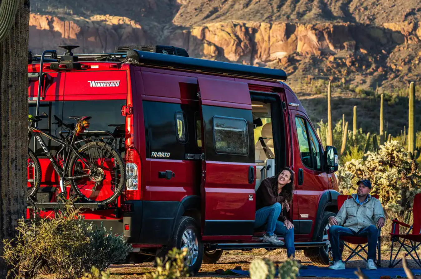 Travelers sit outside their red Winnebago Travat