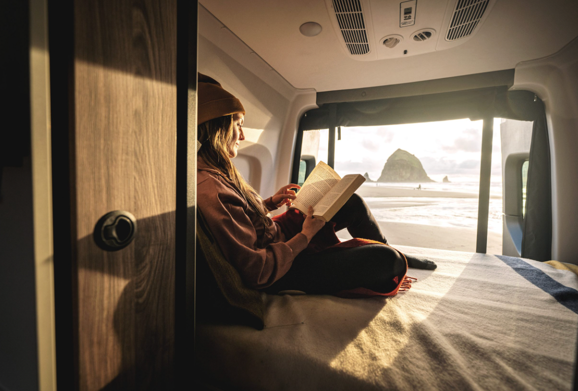 A traveler reads a book in bed on the 2025 Tiffin GH1