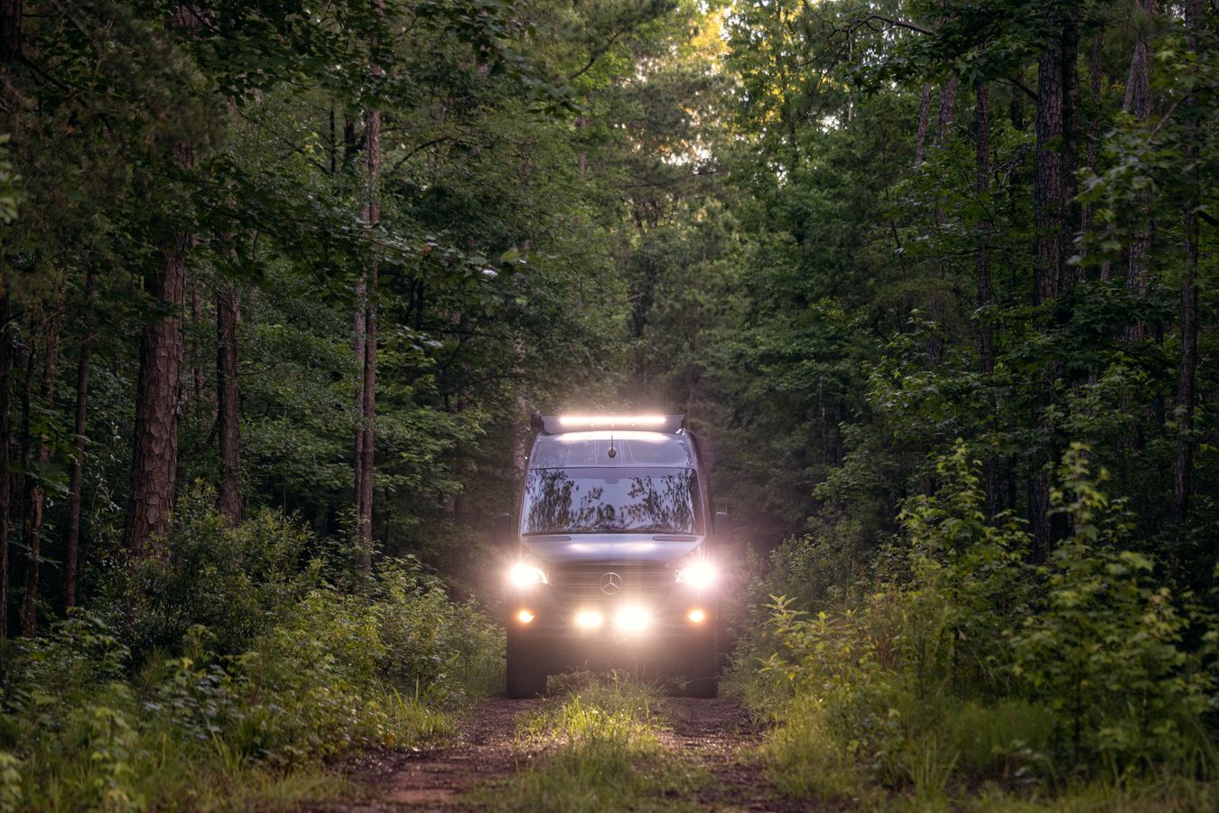 A Tiffin GH2 drives through a wooded area with lights on