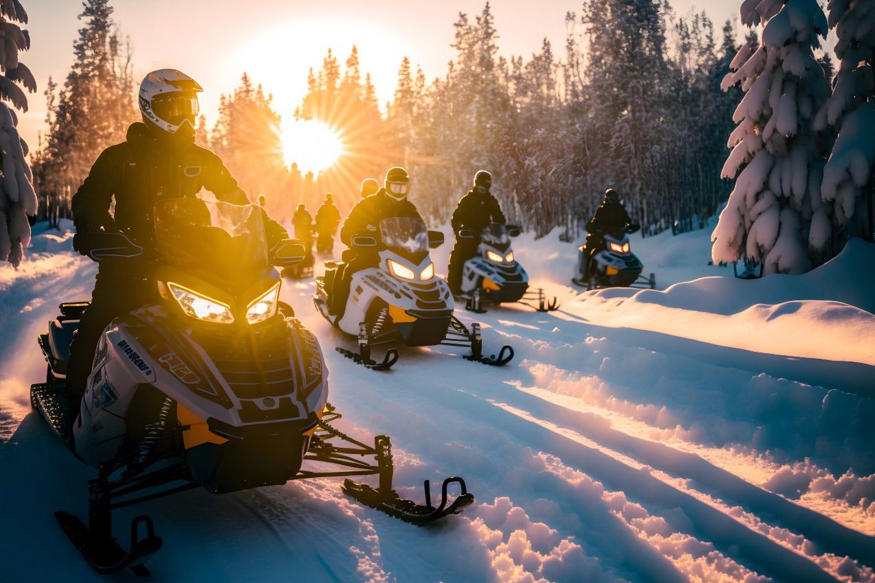 Group of snowmobilers with sun low on the horizon shining through the trees 