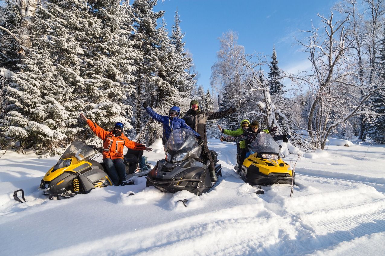 Friends sitting on snowmobiles in fresh snow by a trail