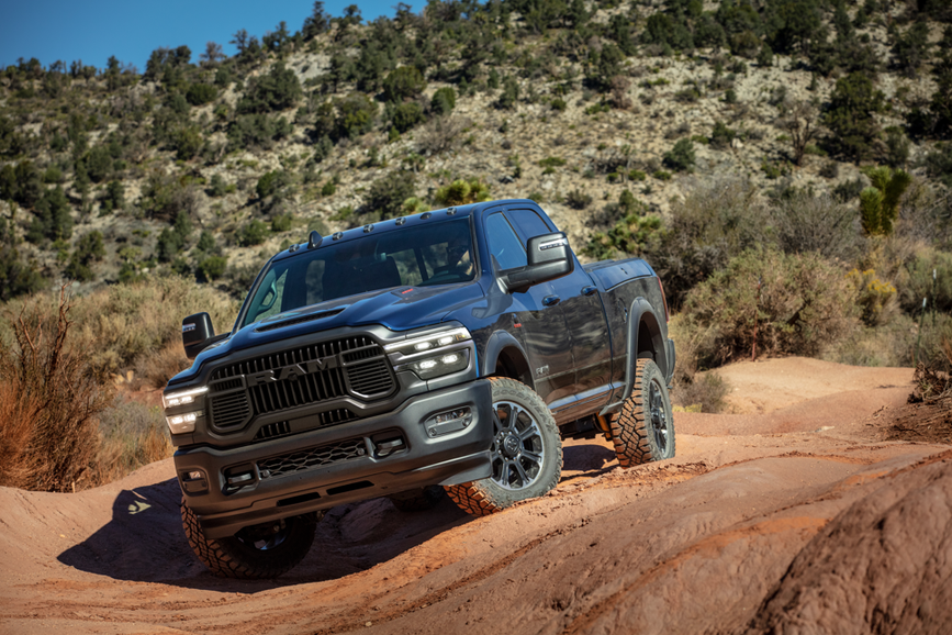 2025 2500 Rebel in Forged Blue off roading on muddy hills, with tall hills and blue sky visible in the distance.