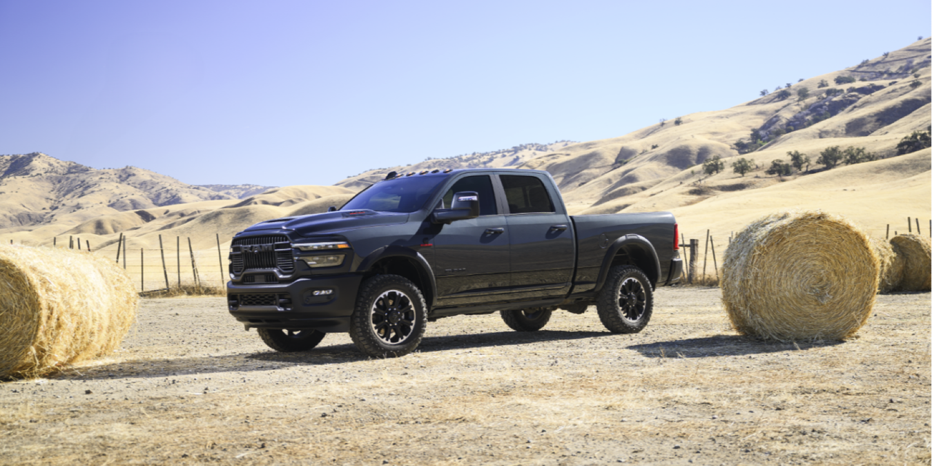2025 2500 Rebel HD in Forged Blue parked in a hay field with desert mountains and clear blue skies visible behind.