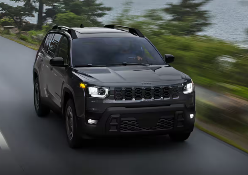 2026 Jeep Cherokee Limited 4x4 driving on a wet road surrounded by trees and water