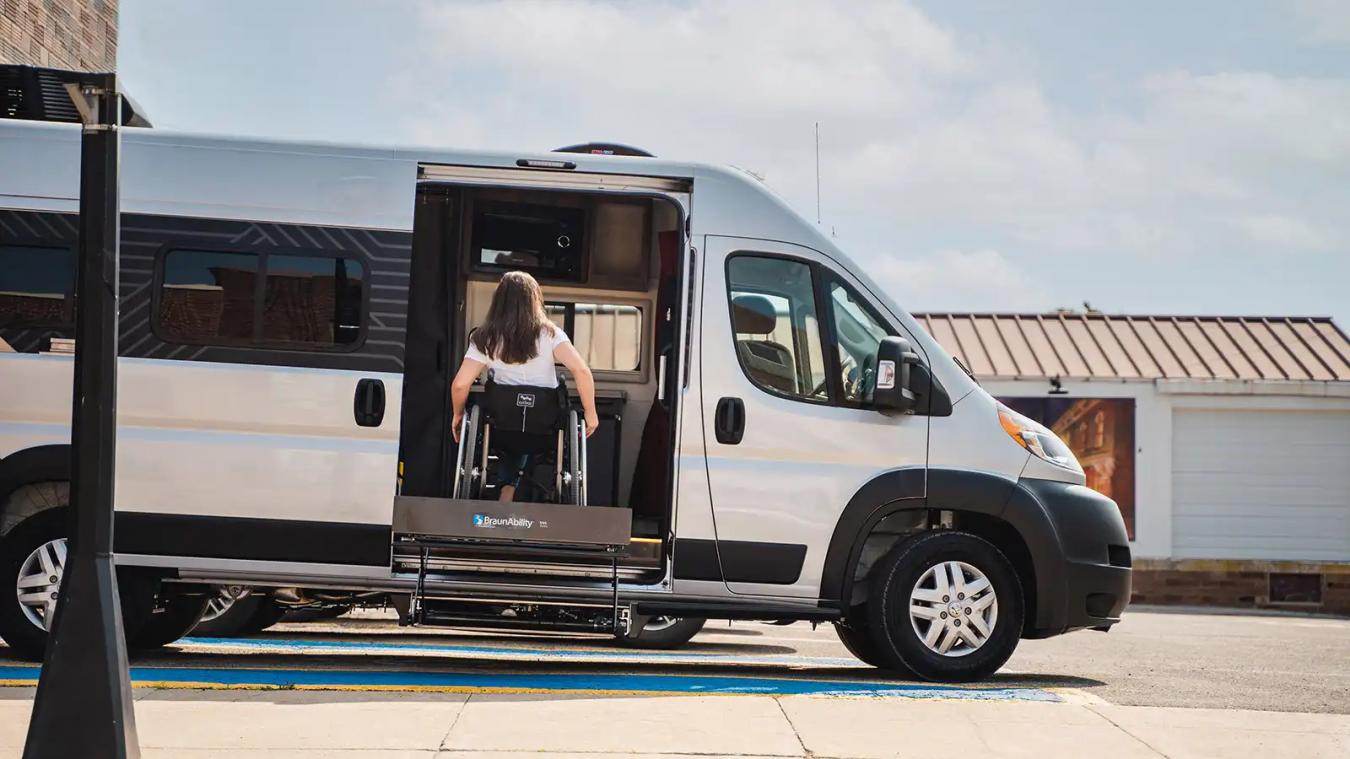 A woman in a wheelchair using a lift to get inside of the Winnebago RV