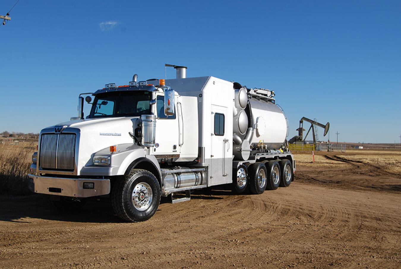 White and grey Foremost hydrovac truck in front of an oil derrick