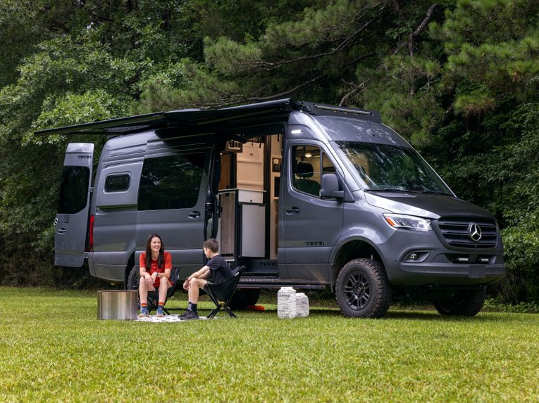 A child and an adult sit outside a 2026 Tiffin GH2 on a sunny day