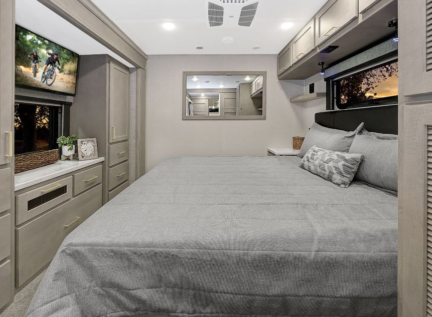 Hallway view of the 2026 Renegade Valencia with dual bunk beds on the left, each with windows and privacy curtains, leading into the back bedroom with a bed and dresser.