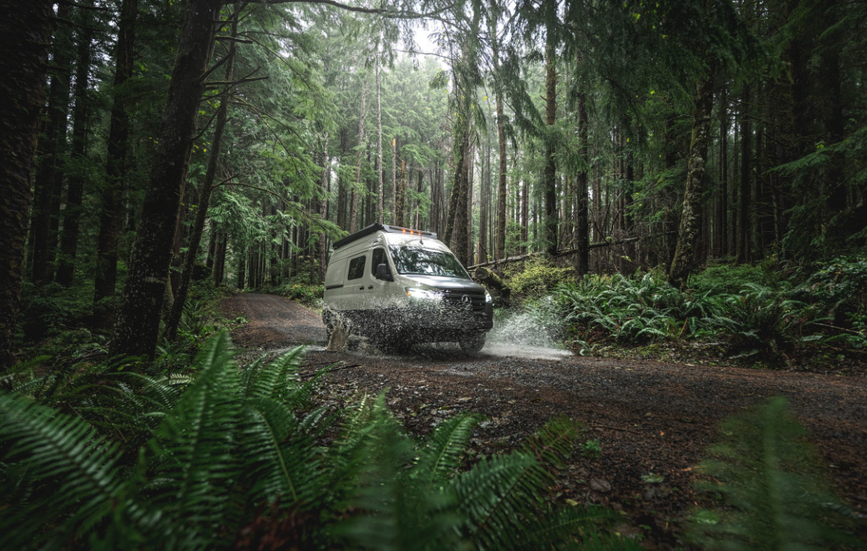 A 2025 Tiffin GH1 drives through a wooded area